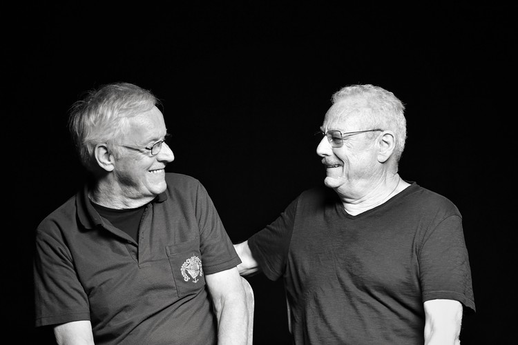 Foto in bianco e nero dei due fratelli Peter e Kurt Bönzli. Sono seduti uno di fronte all'altro e ridono insieme.