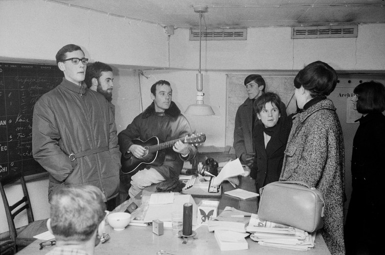 Foto in bianco e nero con al centro il giovane pastore Ernst Sieber, con in mano una chitarra, in una stanza bunker. Altre sei persone sono in piedi o sedute intorno a un tavolo, tutte vestite con abiti invernali. Ascoltano la musica o chiacchierano.